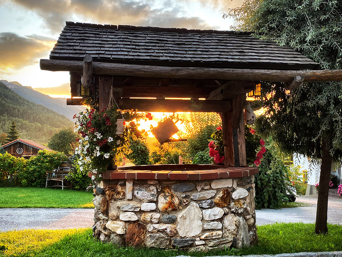 Alter Brunnen mit Blumenschmuck bei der Hofeinfahrt zum Bio-Bauernhof Simonbauer mit Apartments, Ferienhaus, Penthaus und Zimmer in Ramsau am Dachstein